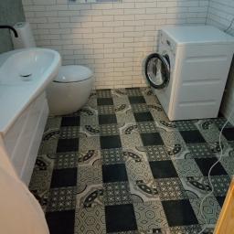 Abc Rusztowania Dawid Saganowski - Nowoczesna łazienka z białą armaturą, pralką i wzorzystą podłogą w odcieniach szarości i czerni, wykończona białymi płytkami imitującymi cegłę.