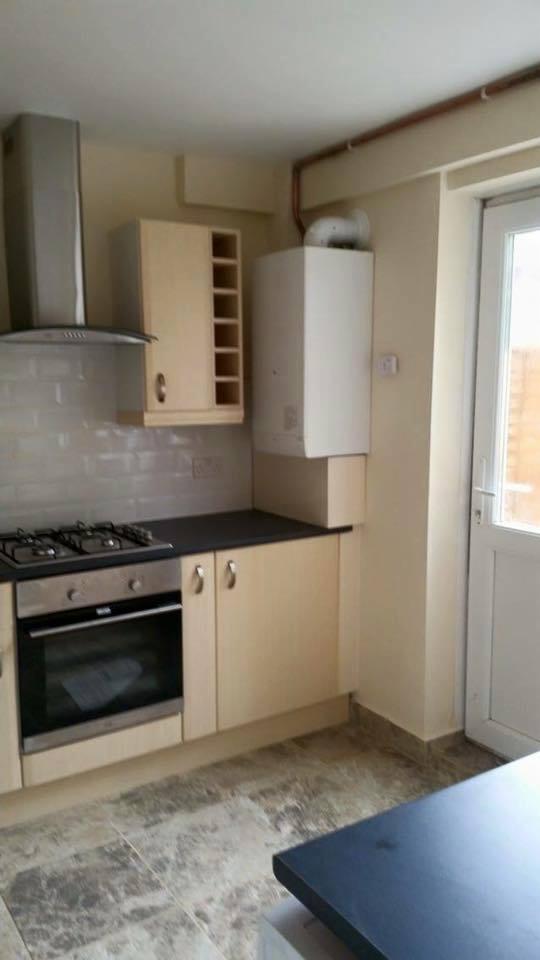 Jasna kuchnia z beżowymi szafkami, płytą grzewczą, piekarnikiem i wiszącym piecem gazowym.