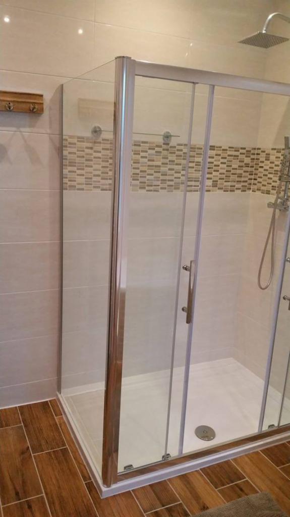 Nowoczesna kabina prysznicowa z przesuwnymi drzwiami, wykończona płytkami w odcieniach beżu i brązu, z drewnopodobną podłogą i chromowaną armaturą.