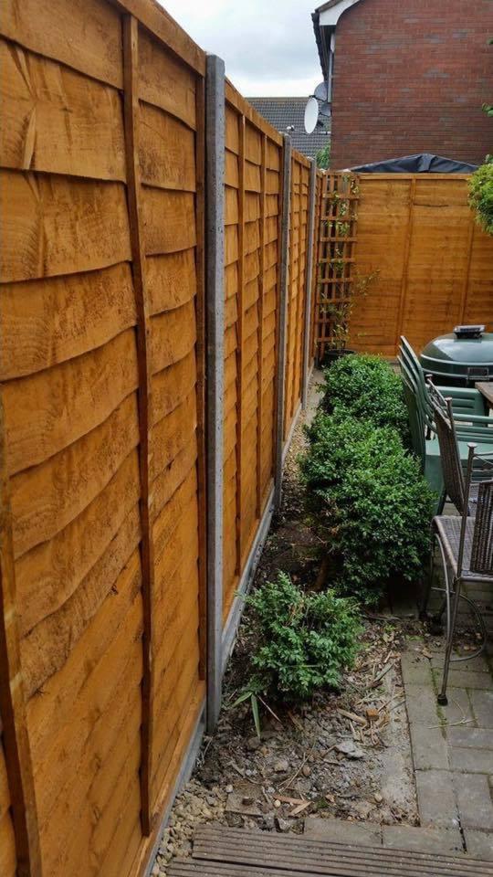 Nowe, drewniane ogrodzenie panelowe z betonowymi słupkami, oddzielające posesję od sąsiada, z widocznymi krzewami i elementami wyposażenia ogrodu.