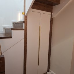 FRED P.P.U - Nowoczesne schody z drewnianymi stopniami i szklaną balustradą, zintegrowane z szafą pod schodami, wykończone w jasnych kolorach i drewnianych akcentach.