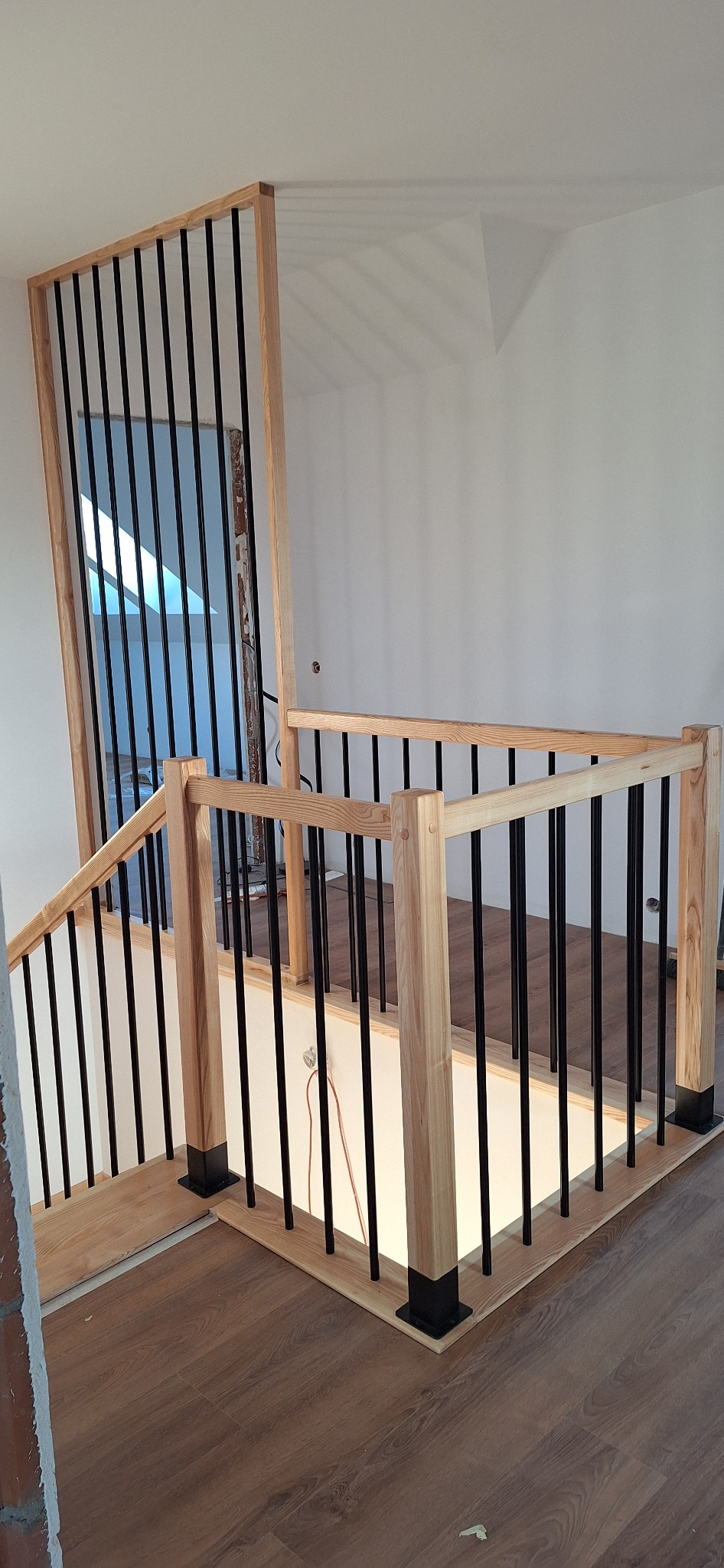 Nowoczesna balustrada schodowa z jasnego drewna i czarnych, pionowych prętów, widok z góry, fragment schodów z drewnianą podłogą, minimalistyczny design.