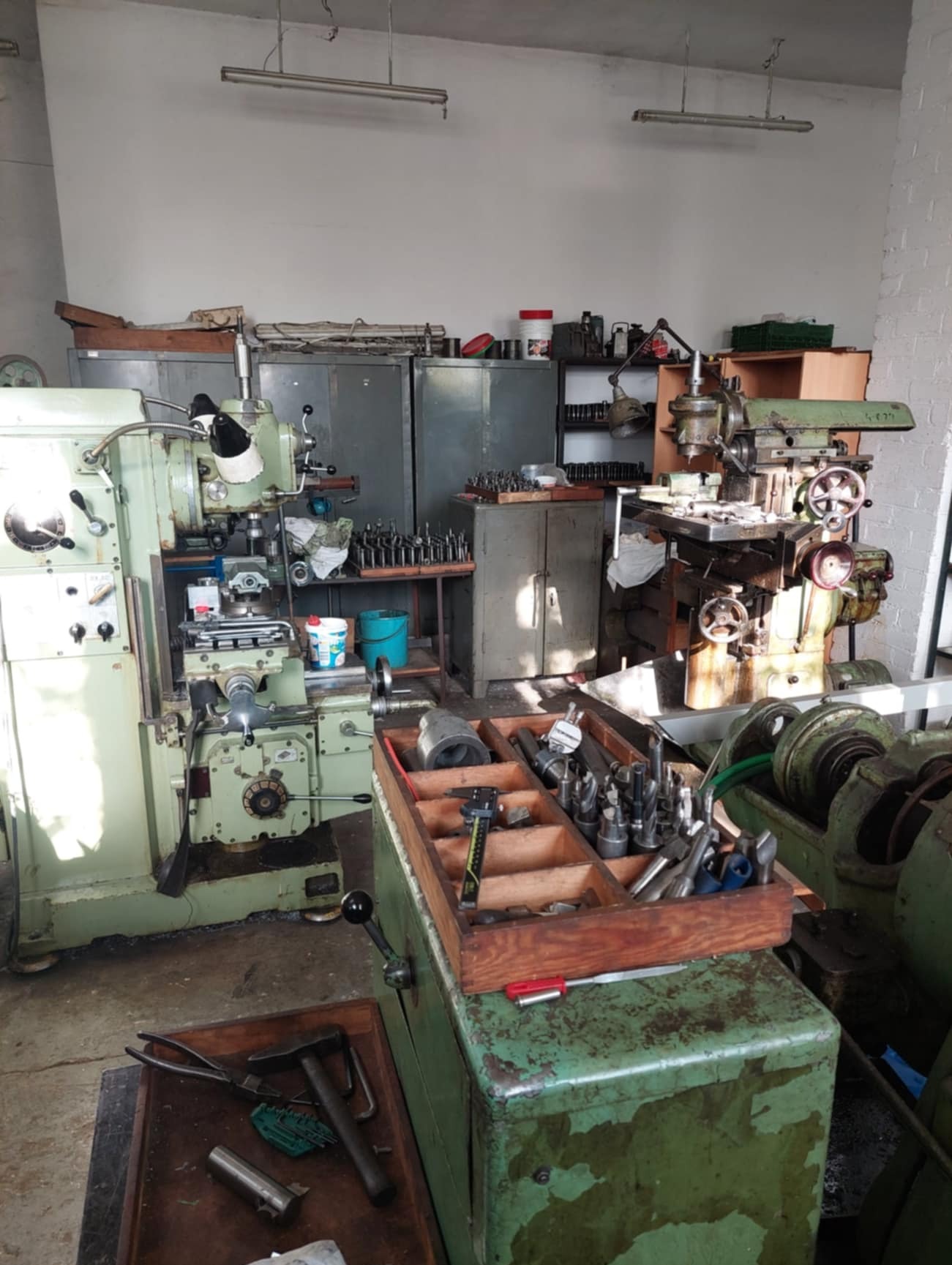 Wnętrze warsztatu obróbki metali z dwoma maszynami: frezarką i tokarką, skrzynką z narzędziami skrawającymi oraz szafkami w tle.