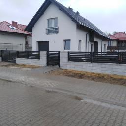 AMB-MET - Nowoczesne, poziome, czarne panele ogrodzeniowe zamontowane na niskim murku z betonowych bloczków w kolorze szarym, na tle nowego domu z białą elewacją i szarym dachem, widok z poziomu ulicy.