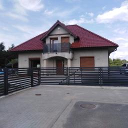 AMB-MET - Nowoczesna posesja w Wołowie z grafitową, poziomą bramą wjazdową i ogrodzeniem panelowym, dopasowanymi do balustrady balkonowej w domu z czerwoną dachówką.