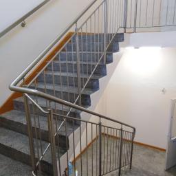 AMB-MET - Schody z szarego lastryko z nierdzewną balustradą, widoczne ślady użytkowania, butelki po napojach i wiadro z mopem na dolnym biegu.