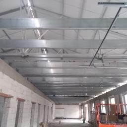 AMB-MET - Wnętrze hali produkcyjnej w trakcie budowy, widoczne surowe ściany z betonu komórkowego, stalowa konstrukcja dachu i podnośnik koszowy.