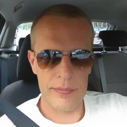 Mężczyzna w okularach przeciwsłonecznych siedzący w samochodzie z zapiętym pasem bezpieczeństwa.