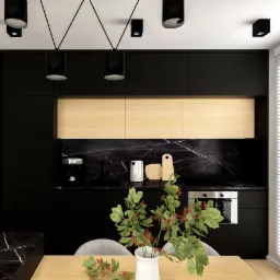 Nowoczesna, czarna kuchnia z marmurowym blatem i drewnianymi szafkami górnymi, oświetlona punktowymi lampami sufitowymi i ozdobiona wazonem z zielonymi gałązkami na drewnianym stole.