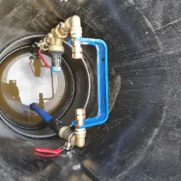 Wnętrze zbiornika z zamontowanymi zaworami, rurami i niebieskim wspornikiem, widoczna woda z odbiciem.