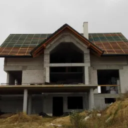 Surowy stan domu jednorodzinnego z częściowo ułożoną dach&oacute;wką w odcieniach zieleni i brązu, widoczny komin, szary dzień w Krakowie.