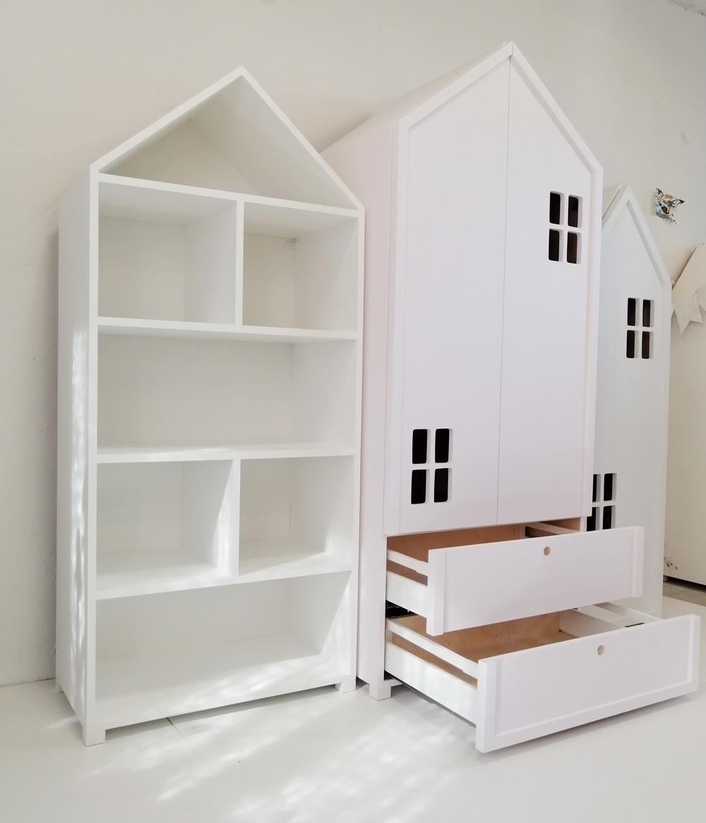 Biała szafa i regał dziecięcy w kształcie domków z otwartymi szufladami, minimalistyczny design, na tle białej ściany i podłogi.