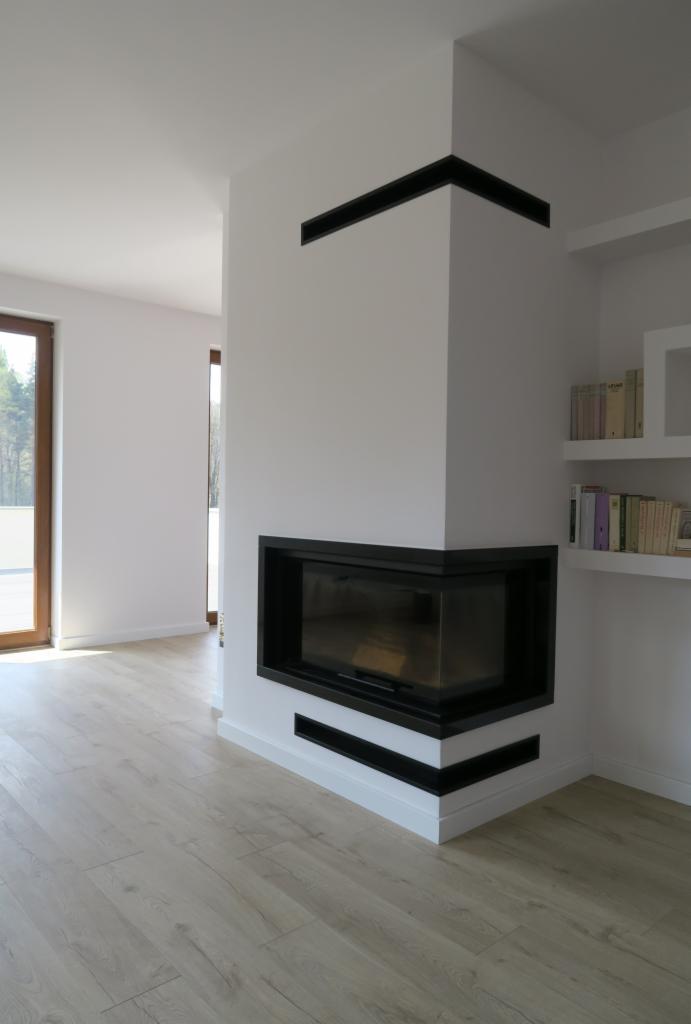 Nowoczesny narożny wkład kominkowy z czarną obudową, w jasnym wnętrzu z półkami na książki.