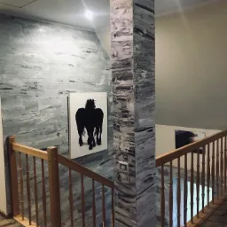 Schody z drewnianą balustradą i kolumną z efektem marmuru, ściana z dekoracyjną fakturą, obraz z sylwetką koni.