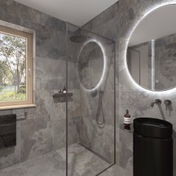 Modei Sztuka & Design - Nowoczesna łazienka z szarymi płytkami imitującymi kamień, okrągłym lustrem z podświetleniem LED i czarną umywalką nablatową. Widok na zieleń za oknem.