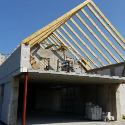 Budowa domu murowanego: surowy stan z widoczną więźbą dachową, ściany z betonu kom&oacute;rkowego i widoczne rusztowania wewnątrz, błękitne niebo w tle.