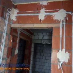 Montaż instalacji elektrycznej w budynku z czerwonej cegły, kable prowadzone wzdłuż ścian, zabezpieczone gipsem