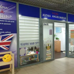 Wejście do szkoły językowej z plakatem 'Do You speak English?', numerem telefonu i dekoracją sowy na książkach na szklanych drzwiach.