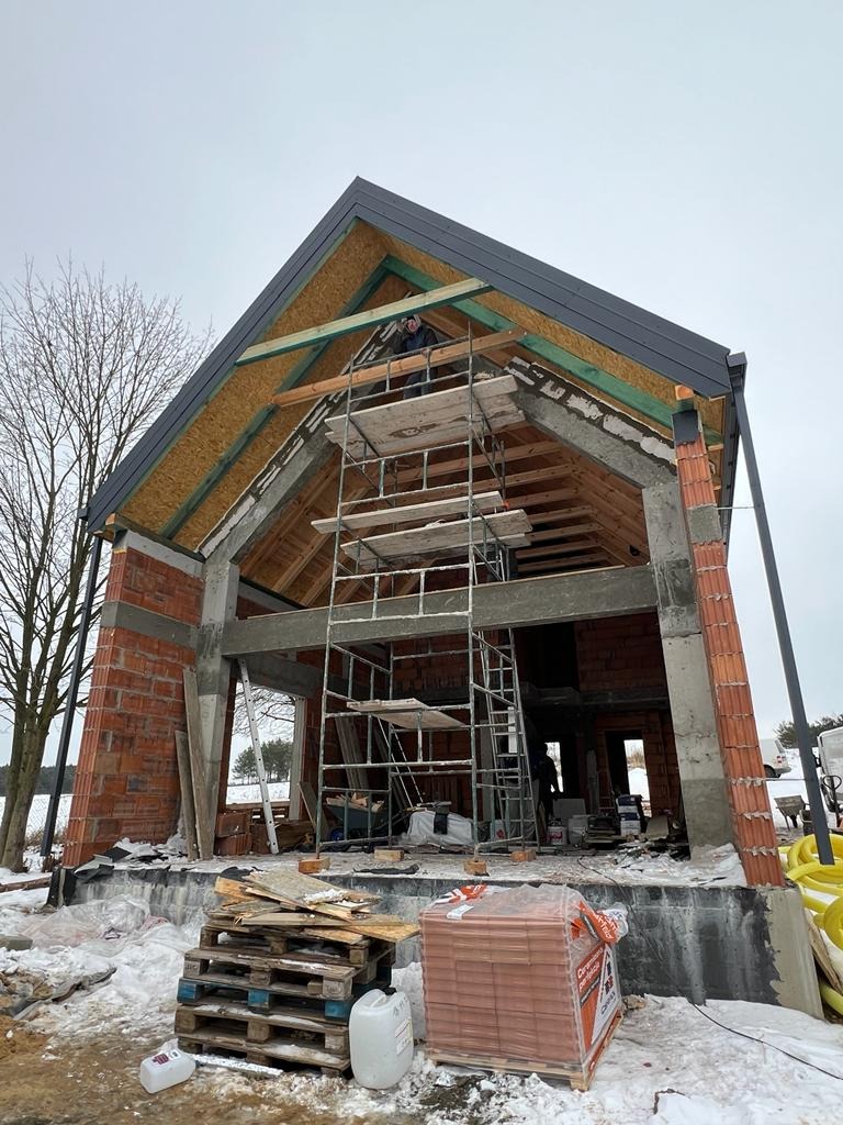 Budowa domu jednorodzinnego w Turkowy w trakcie realizacji, widoczne ściany z cegły, rusztowanie i konstrukcja dachu z deskowaniem.