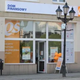 Fasada budynku 'Dom Finansowy' z pomarańczowymi balonami i plakatami reklamującymi pożyczki oraz kredyty, oświetlona latarnią uliczną.