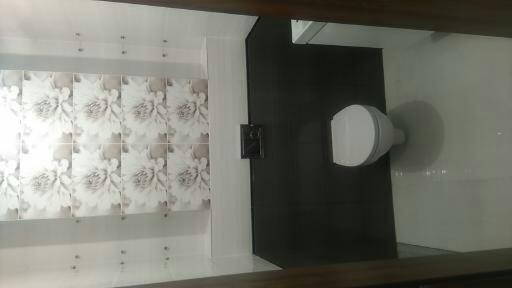 Wykończona łazienka z czarnymi płytkami na ścianie i białym sedesem, na ścianie z lewej strony widoczne płytki z motywem kwiatowym, płytki zamontowane z użyciem krzyżyków dystansowych.