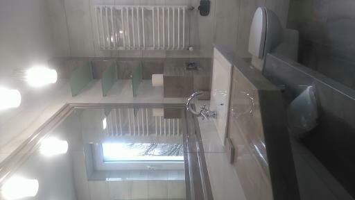 Nowoczesna łazienka z szarymi i białymi płytkami, grzejnikiem drabinkowym, szklanymi półkami i oknem dachowym.