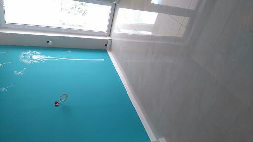 Błękitna ściana z motywem dmuchawca i lśniąca, jasna podłoga z płytek w nowoczesnym wnętrzu, widok z góry