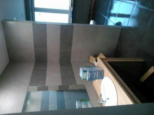 Wykończona łazienka z szarymi płytkami ułożonymi w pionowe pasy, widoczna umywalka na drewnianym blacie i kartony z materiałami budowlanymi.