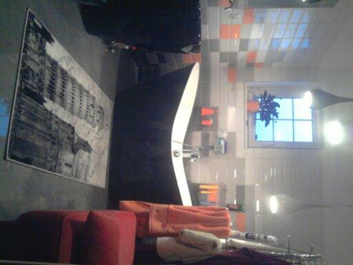 Nowoczesna łazienka z biało-szarą glazurą, pomarańczowymi akcentami i dużym obrazem na ścianie, widok z góry.