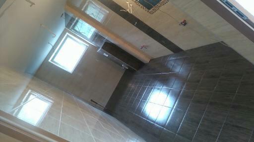 Wykończona łazienka z ciemnymi, błyszczącymi płytkami podłogowymi i jasnymi płytkami na ścianach, widoczne dwa okna wpuszczające naturalne światło.