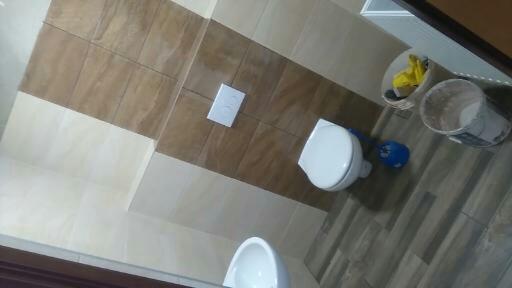 Wykończona łazienka z brązowo-beżowymi płytkami na ścianach i podłodze, widoczny fragment umywalki, toaleta, spłuczka podtynkowa i wiadro z akcesoriami malarskimi.