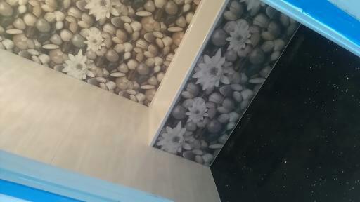 Wykończona łazienka z płytkami imitującymi kamienie i kwiaty na ścianie oraz czarnymi błyszczącymi płytkami na ścianie obok.