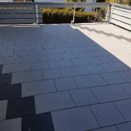 Wyłożony szarymi płytkami taras z dekoracyjnym pasem z czarnych płytek, widok z góry w słoneczny dzień.