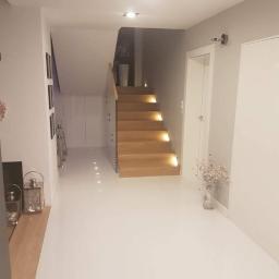 MEGA BUD Arkadiusz Zakrzewski - Nowoczesny przedpokój z drewnianymi schodami podświetlonymi od spodu, jasna podłoga z połyskiem, minimalistyczne dekoracje.