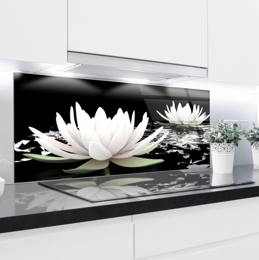 Szklany panel kuchenny z motywem białych lilii wodnych na czarnym tle, zamontowany nad płytą indukcyjną w nowoczesnej kuchni z białymi szafkami.