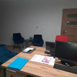 Biuro w Radlinie z biurkiem, komputerami, dokumentami i krzesłami w odcieniach niebieskiego i czerwonego, gotowe do pracy księgowej.