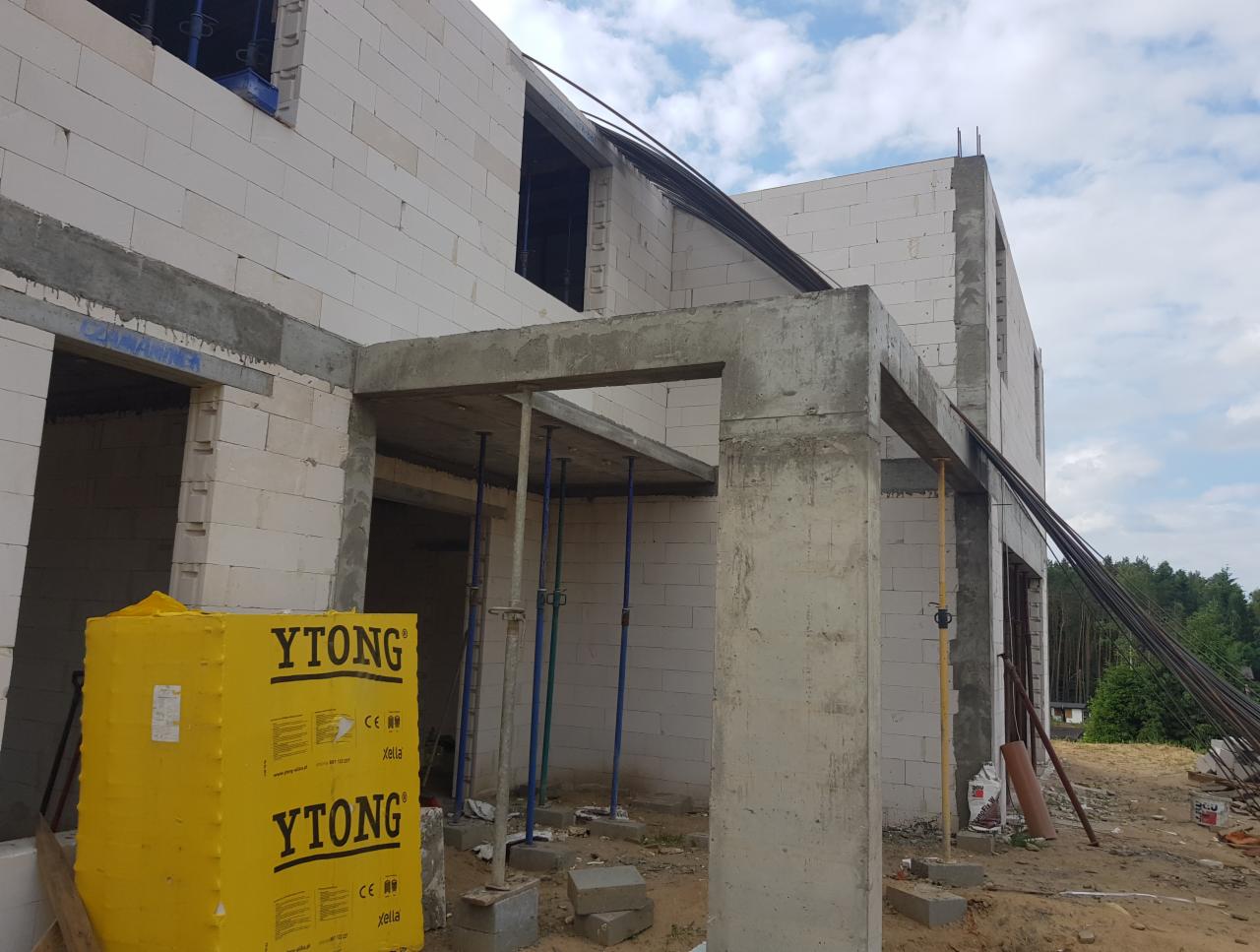 Wznoszenie domu murowanego z betonu komórkowego Ytong, widoczne zbrojenia i podpory szalunkowe, teren budowy w trakcie prac.