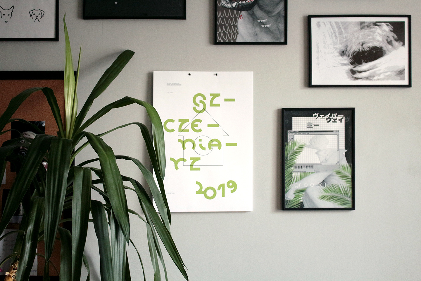 Ściana z galerią plakatów w czarnych ramkach, w tym minimalistyczny plakat z zielonym napisem 'SZCZENIARZ' i graficznym symbolem domu, oraz duża roślina doniczkowa z długimi, zielonymi liśćmi po...
