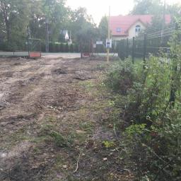 RBN Polska Sp. z o.o. - Teren po wycince drzew i krzewów, widoczne ślady opon na ubitej ziemi, ogrodzenie z siatki i brama w tle, domy w oddali.