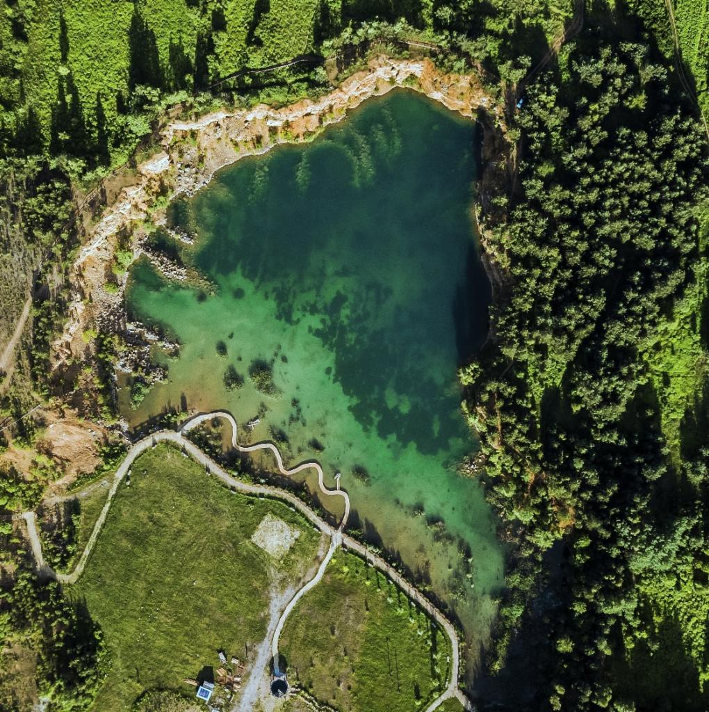 Widok z lotu ptaka na malownicze jezioro z krętą ścieżką wzdłuż brzegu, otoczone zielenią drzew i trawników.