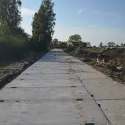 Ułożona tymczasowa droga z szarych płyt betonowych na placu budowy, widok z perspektywy pieszego, lekko z prawej strony, z widocznymi śladami ziemi po bokach i błękitnym niebem w tle.