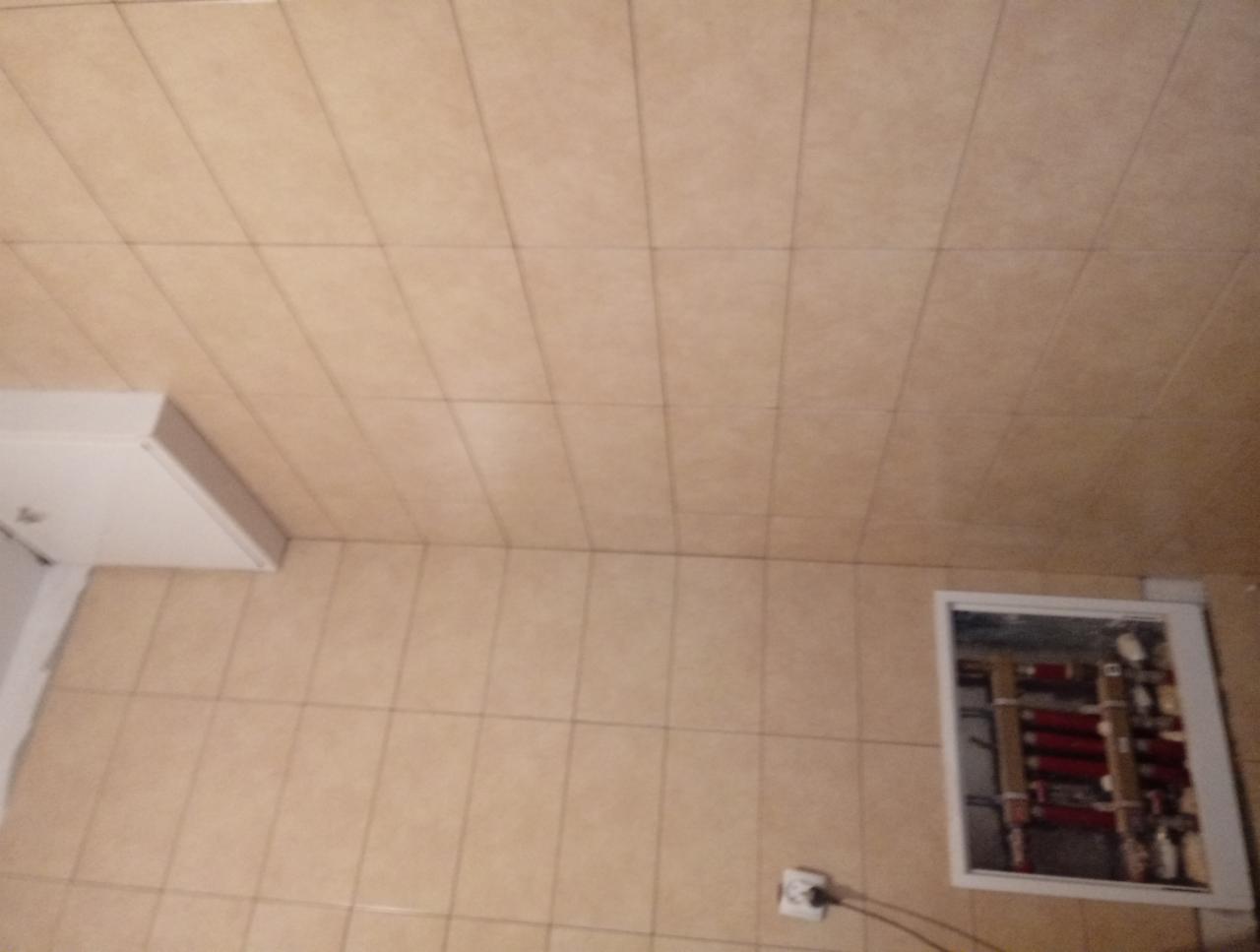 Beżowe płytki ceramiczne na ścianie i suficie łazienki, widoczna klapa rewizyjna z instalacją hydrauliczną i gniazdko elektryczne