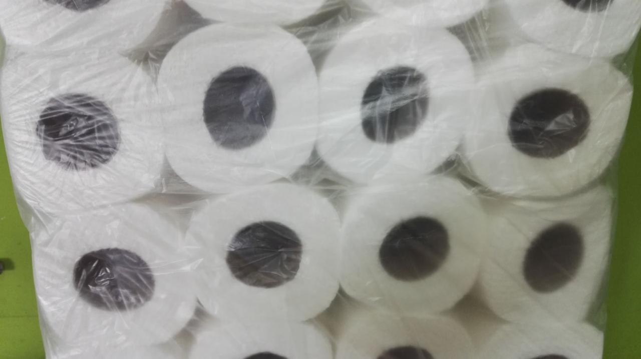 Wielopak rolek białego papieru toaletowego zapakowany w przezroczystą folię, widoczne ciemne otwory rolek.