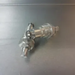 Precyzyjnie obrobiony, metalowy element z gwintowanymi połączeniami, leżący na metalowej powierzchni. Widoczne ślady obróbki.