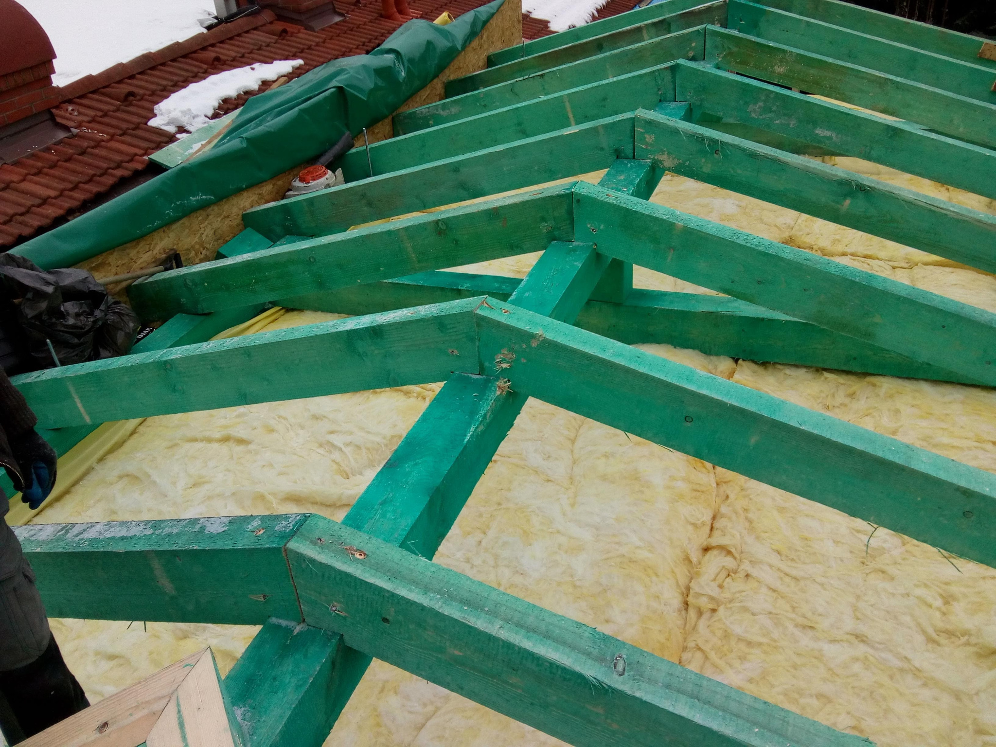 Konstrukcja dachu z zielonych belek drewnianych i izolacją z wełny mineralnej, widok z góry na etapie budowy.