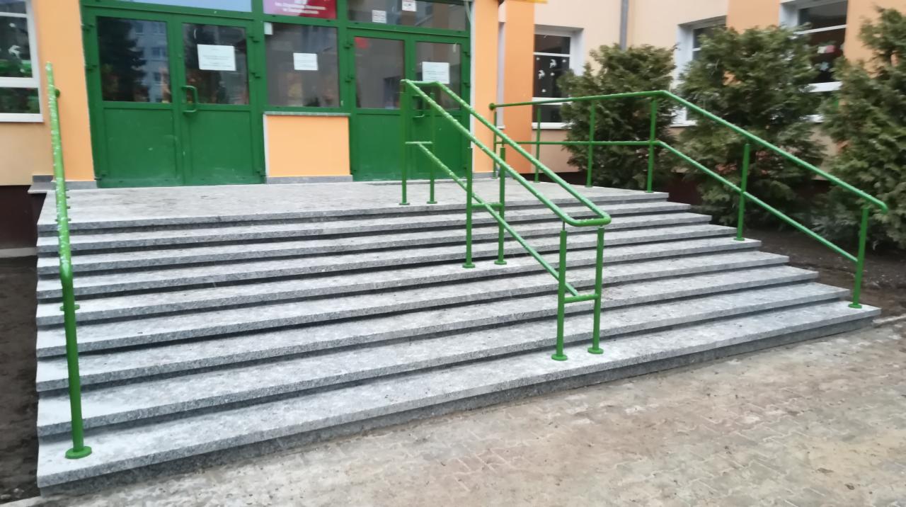 Granitowe schody wejściowe z zielonymi poręczami prowadzące do budynku w Świebodzinie.