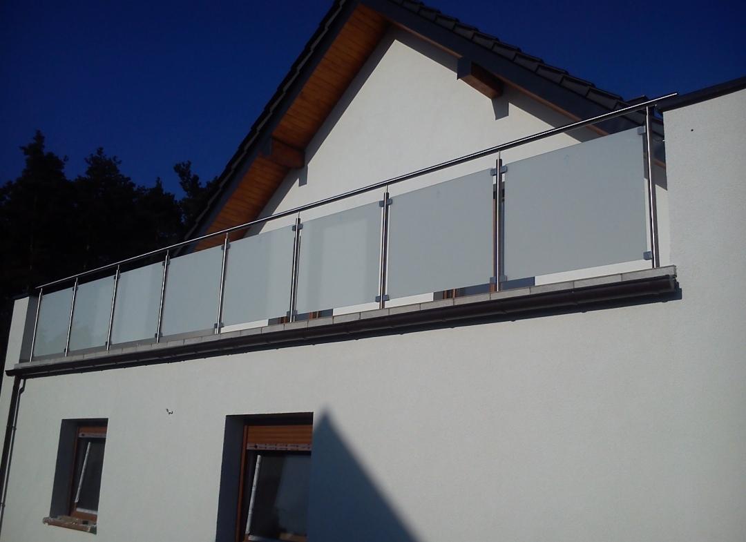 Balkon z nowoczesną balustradą ze stali nierdzewnej i matowego szkła, widok z dołu na tle białej ściany budynku i ciemnego nieba.