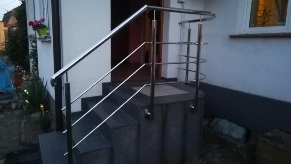 Zewnętrzne schody z czarnego granitu z balustradą ze stali nierdzewnej z zaokrąglonym górnym elementem i poziomymi poprzeczkami, widok z dołu.