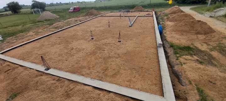 Wylane fundamenty pod budowę domu jednorodzinnego na działce z widocznymi sterczącymi prętami zbrojeniowymi i wykopem obok.