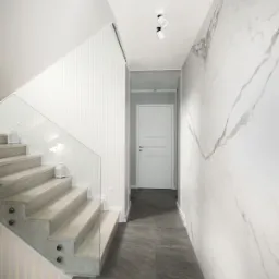 Nowoczesne schody z drewnianymi stopniami i szklaną balustradą, oświetlone lampionami, prowadzące wzdłuż ściany z marmurowym wzorem, widok z dołu.